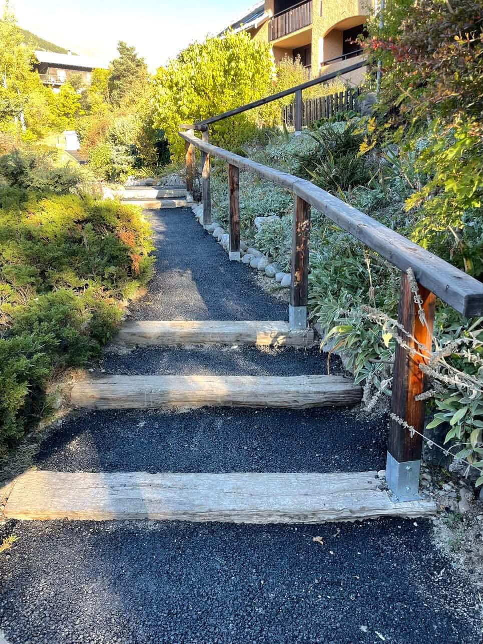 Allée en gravier avec marches et rampe en bois à travers la végétation